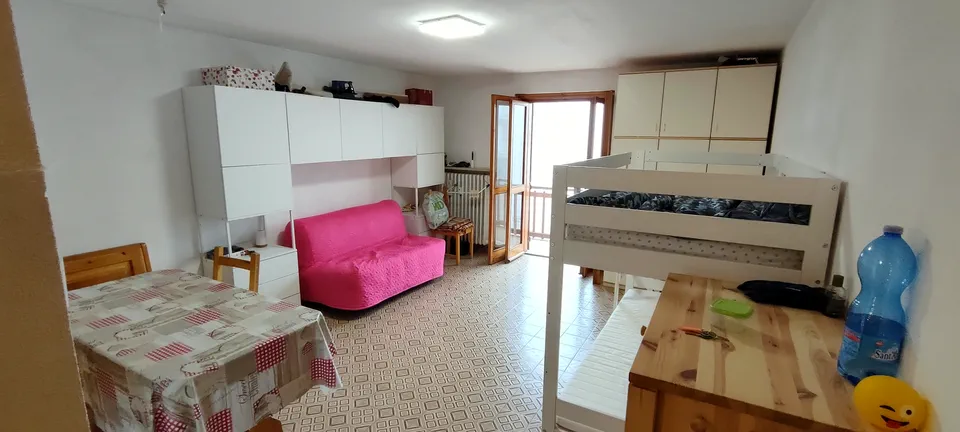 Soggiorno con armadiatura bianca, divano letto, letto a castello e tavolo da pranzo